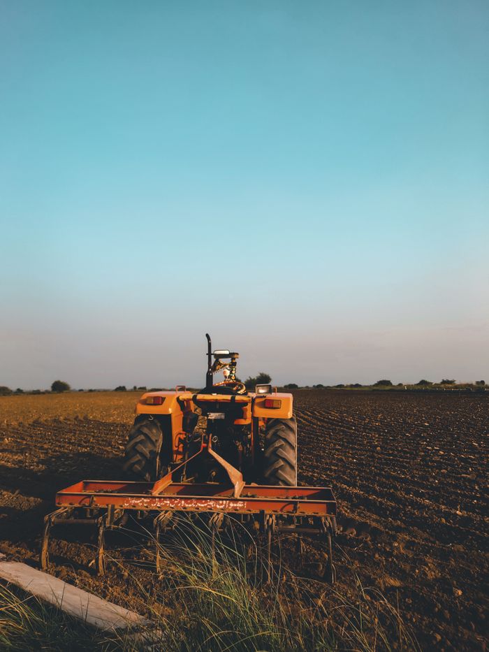 An old tractor in a vast agricultural field at sunset, capturing rural life and farming essence.